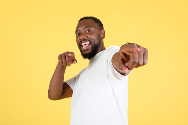 Black guy pointing fingers looking at camera over yellow\
background