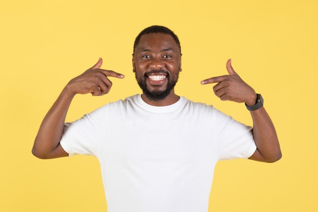 Black Guy Pointing At Himself Smiling To Camera Yellow Background