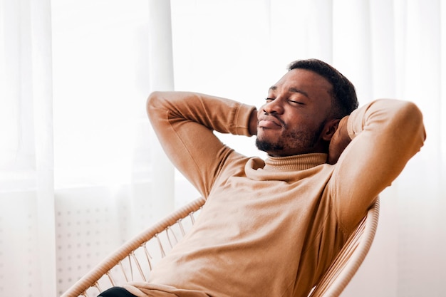 black guy relaxing sitting on modern chair against window indoor
