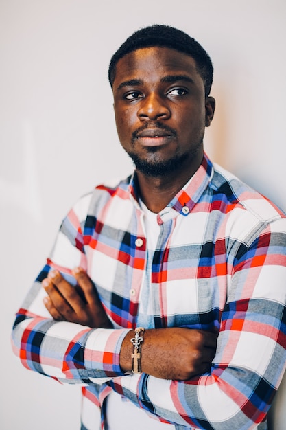 Black guy in shirt posing on white wall.