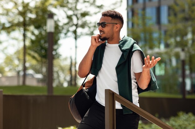 Black guy talking on cellphone outdoors having emotional conversation and gesturing walking outdoors in park