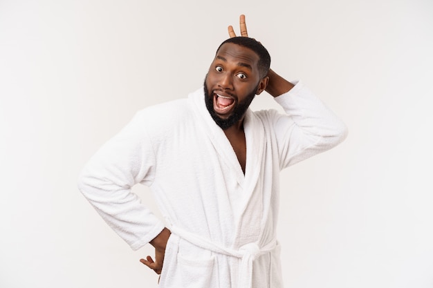 Black guy wearing a bathrobe pointing finger with surprise and happy emotion. Isolated.