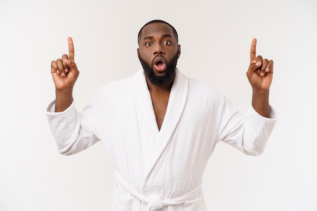 Black guy wearing a bathrobe pointing finger with surprise and happy emotion. 