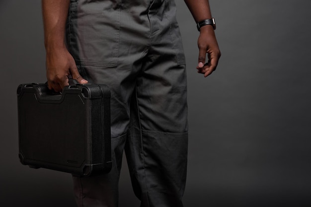 Black guy with a watch on his arm carries a heavy suitcase with wrenches