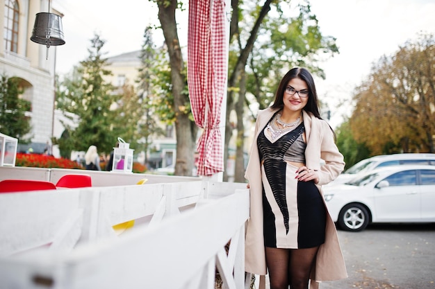 Black hair sexy woman in glasses and coat posed on street