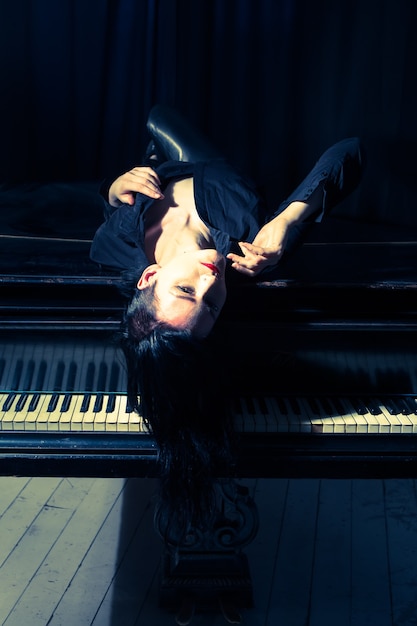 Foto una donna dai capelli neri sdraiata su un pianoforte nero