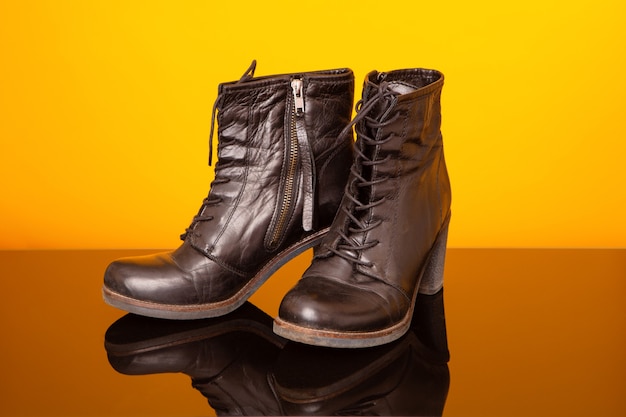 Black half boots with high heel on black glass table and yellow