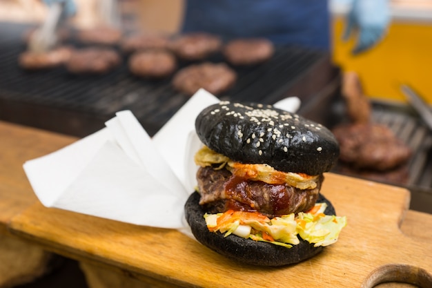 Photo black hamburger and a white paper napkin on a wooden cutting board, japanese culinary specialty colored with additives as bamboo charcoal and squid ink, close-up