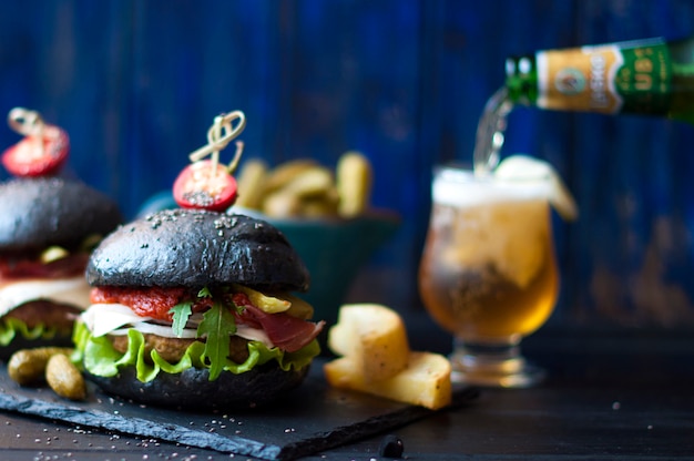 Black hamburger with beef, salad and French fries. Fresh beer in a glass. Trends of street food. A calorie dinner. Copy space