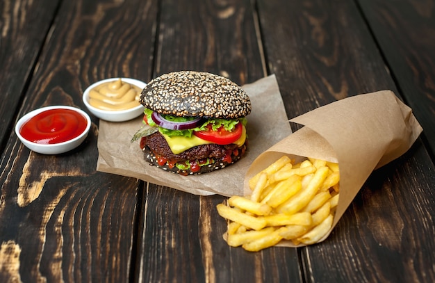 black-hamburger with lettuce, tomatoes and fries. Wooden background