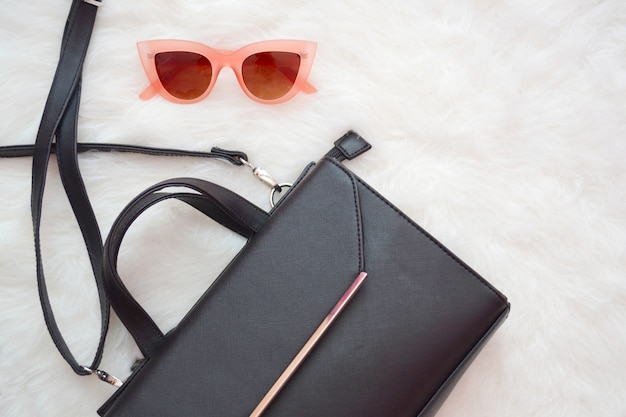 Photo black handbag and pink glasses on a white fur