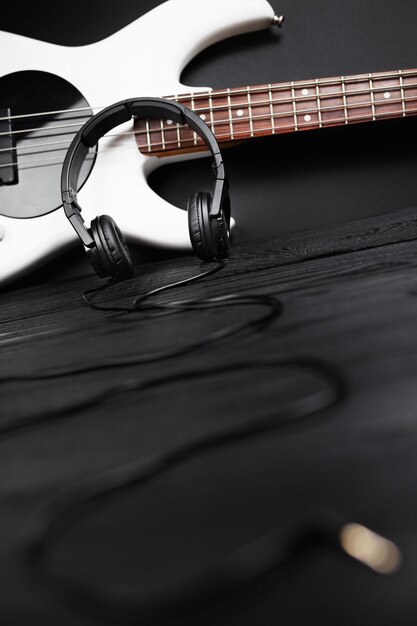 Photo black headphones and white bass guitar on the black wooden background