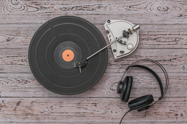 Black headphones with wire and a vintage grey vinyl record player on a wooden background. Retro technique for playing music.