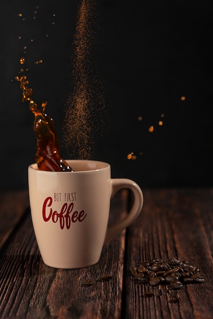 Black hot coffee splashing in beige cup and cinnamon powder falling on dark wooden table with beans