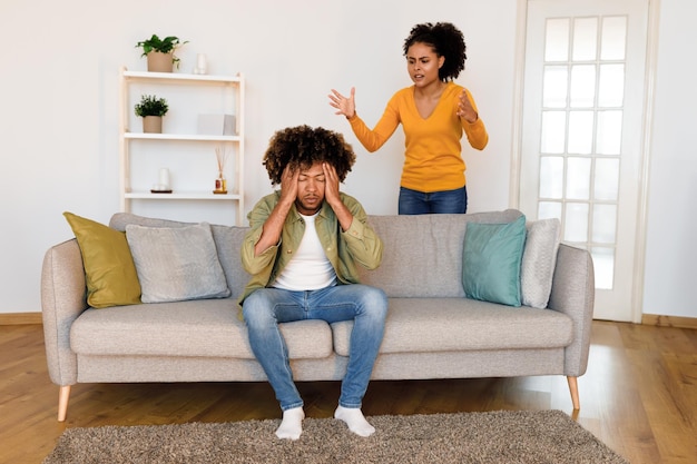 Black husband covers ears as wife shouts during quarrel indoor