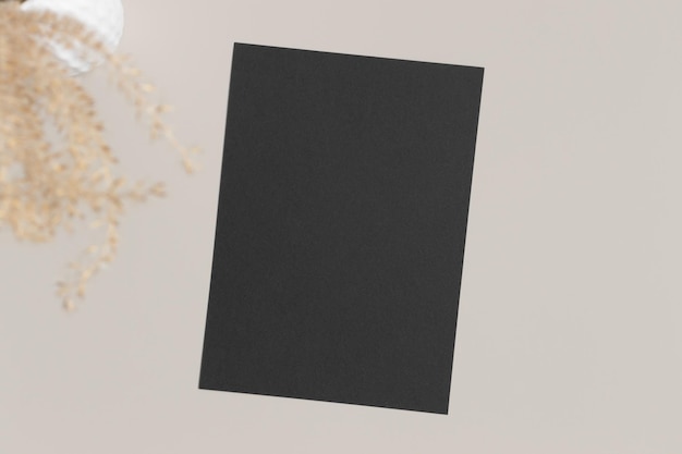 Photo black invitation card mockup with a dried grass on a beige table 5x7 ratio similar to a6 a5