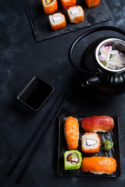 black iron teapot and sushi set on slate plate on black stone table, flat lay