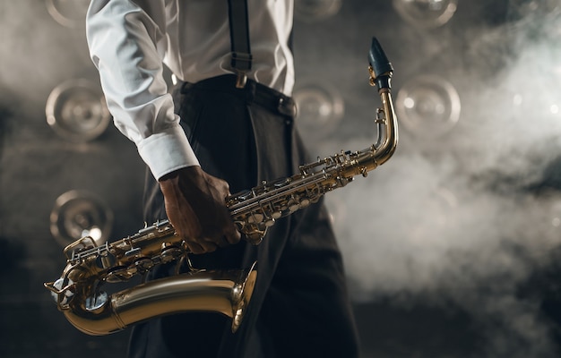 Foto musicista jazz nero con sassofono sul palco con fumo. il jazzista nero tiene lo strumento in mano