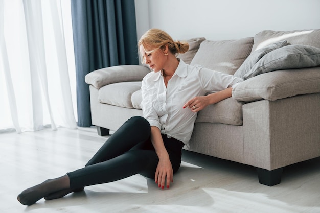 In black jeans woman in formal wear sitting on the floor near
sofa in domestic room