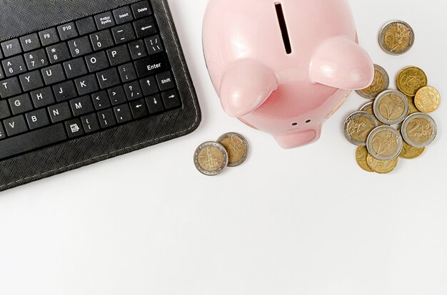 Black keyboard and money box with euro coins on white wall. Saving money concept. Top view, copy space.