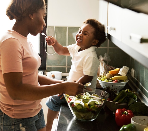 Черный ребенок кормит мать с приготовлением пищи на кухне
