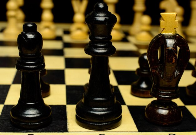 Black king, queen and bishop are standing in a row on a\
chessboard.