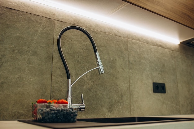 Black kitchen faucet on the silver sink near the glass of water