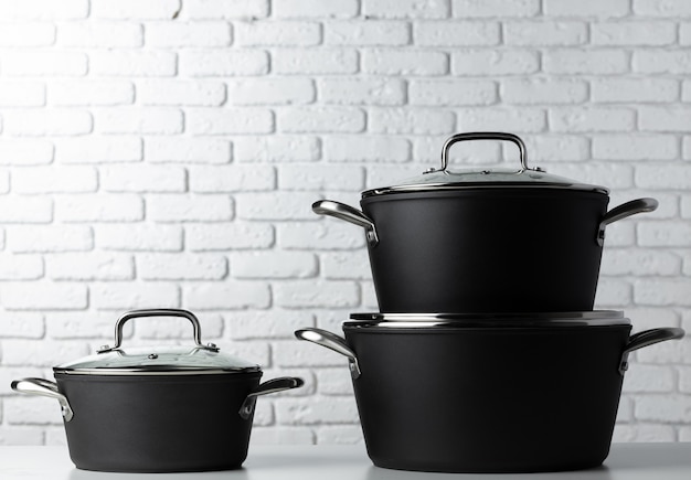 Black kitchenware on table against white brick wall