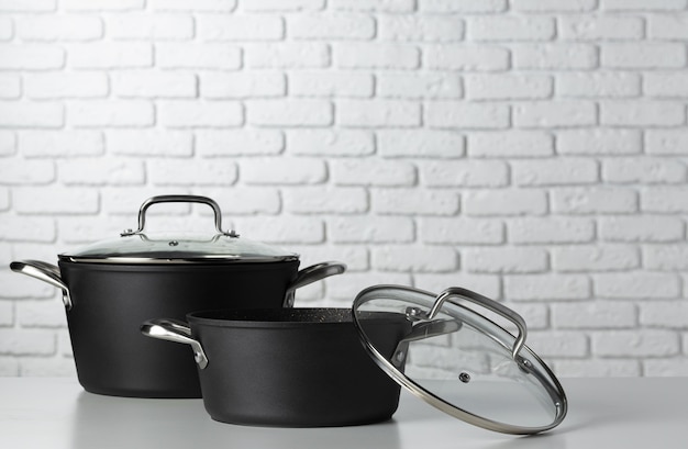 Black kitchenware on table against white brick wall