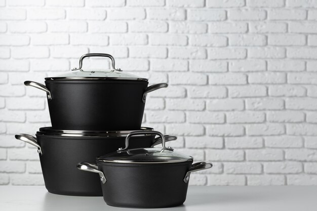 Black kitchenware on table against white brick wall