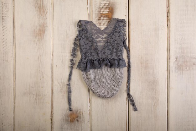 A black lace vest with a grey lace trim hangs on a wooden wall.