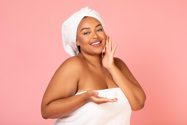 Black Lady Holding Moisturizer crème aanbrengen op gezicht roze achtergrond