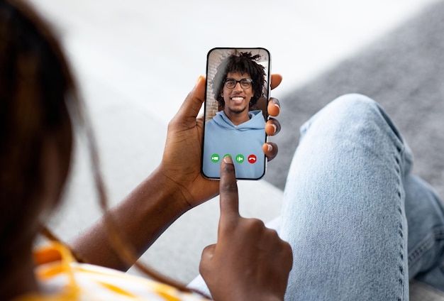 Black lady holding smartphone and making video call with her boyfriend relaxing on couch at home