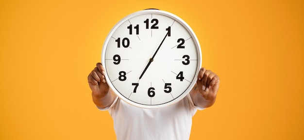 Black lady poses with clock covering head against orange background