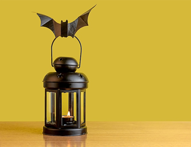 Photo a black lantern stands on the table. a black paper bat sits on the lantern. decoration for the holiday.