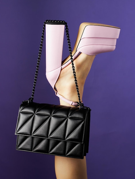 Black leather bag hangs on high heel of pink shoe put on leg