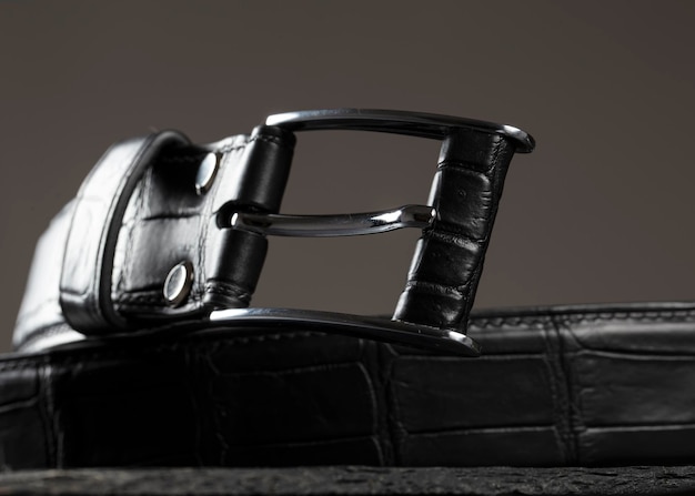 Photo black leather belt with a metal plaque closeup on a gray background