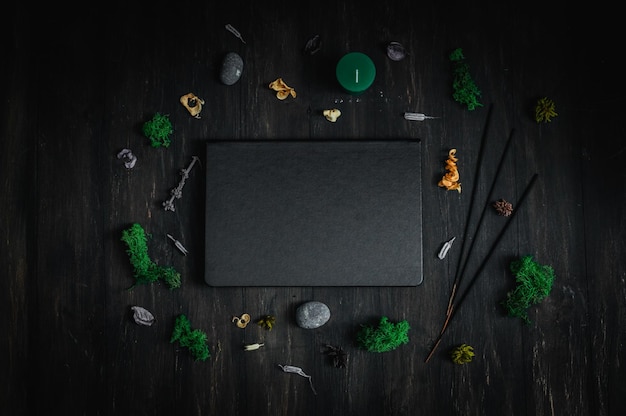 Foto libro in pelle nera con pietre rituali e fiori secchi su fondo nero