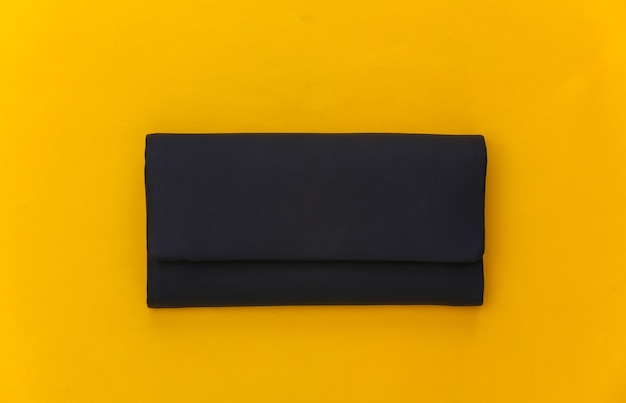 Black leather female clutch handbag on yellow background. Top view