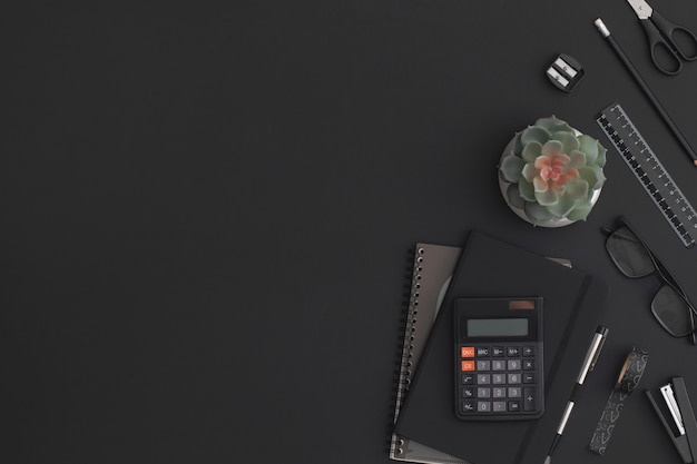 Black leather office table with calculator, notebook, stationery and green plant. Top view with copy space. Flat lay composition.