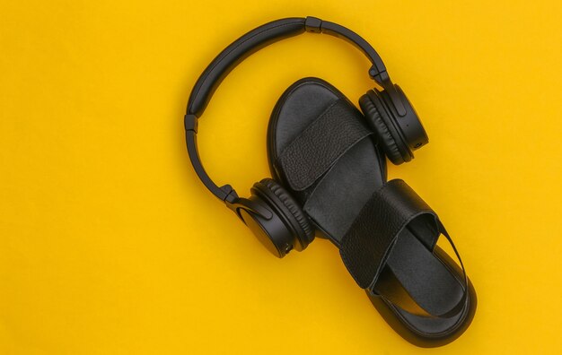 Black leather sandal and stereo headphones on yellow background. Top view