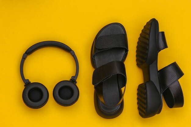 Black leather sandals and stereo headphones on yellow background. Top view