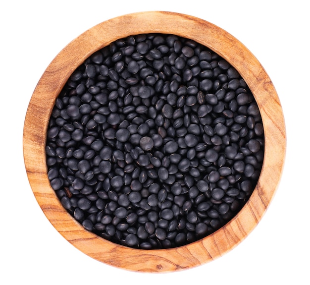 Black lentils in olive bowl isolated on white background Dry beluga lentil grains pile Top view