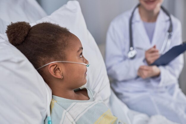 Photo black little girl laying in bed in hospital room