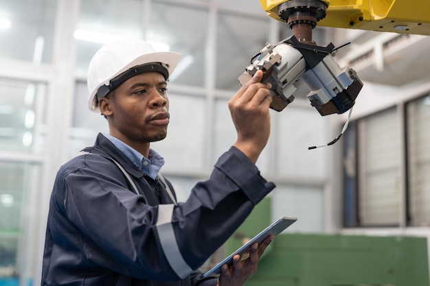 Photo black male automation engineer using tablet checking head welding robot arm machine in factory