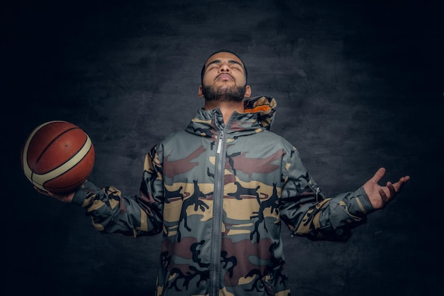 A black male in a camouflage hoodie holds basket ball.