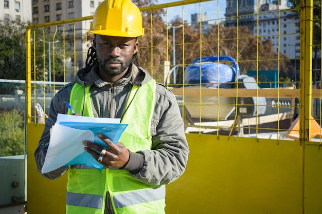 Black male engineer at a construction site outdoors with holding a folder looking at the camera