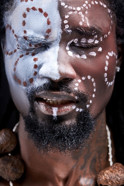 痛みを感じている黒人男性、スタジオで隔離された目を閉じて立っている、顔に絵を描いている、民族の国民の化粧