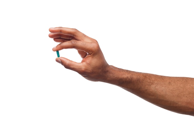 Black male hand holding a pill between thumb and forefinger isolated on white background. Health care, treatment concept