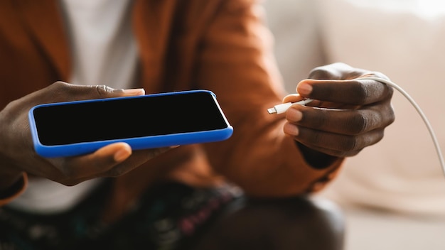 Black male hands plugging a charger in modern smartphone using powerbank closeup